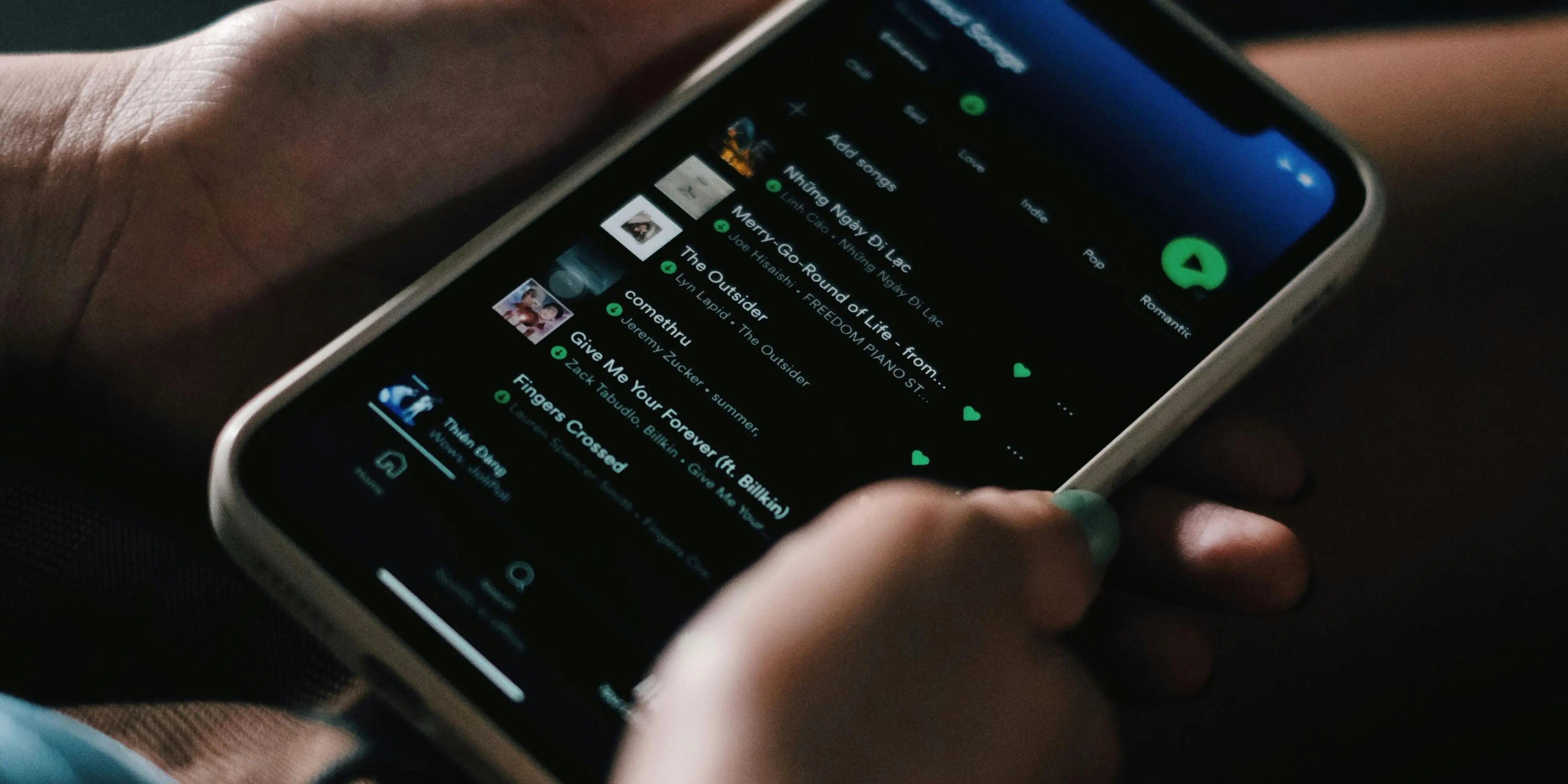 A man is holding his phone with a Spotify playlist shown on the screen.