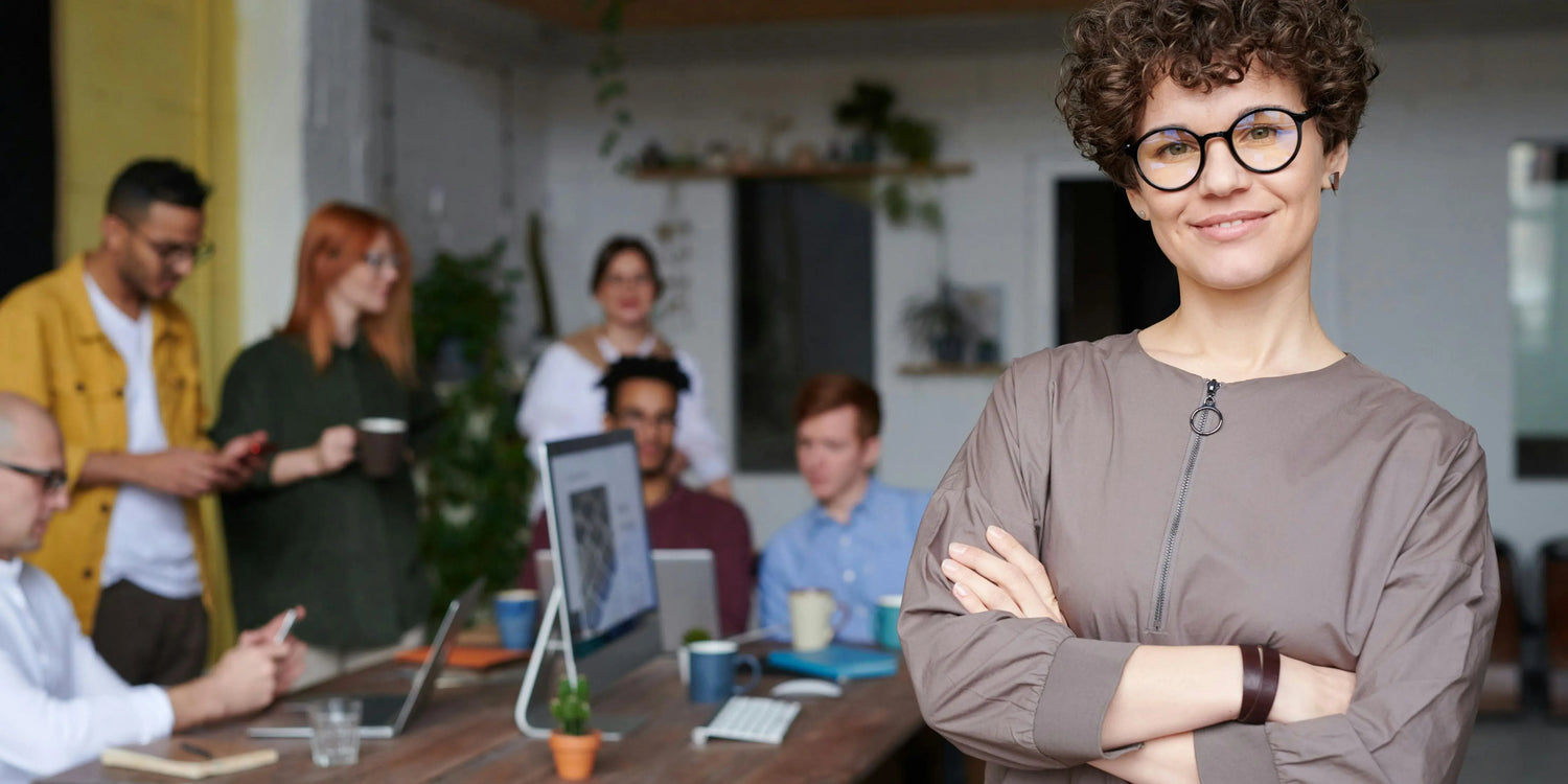 A woman stands smiling in front of her team in an office