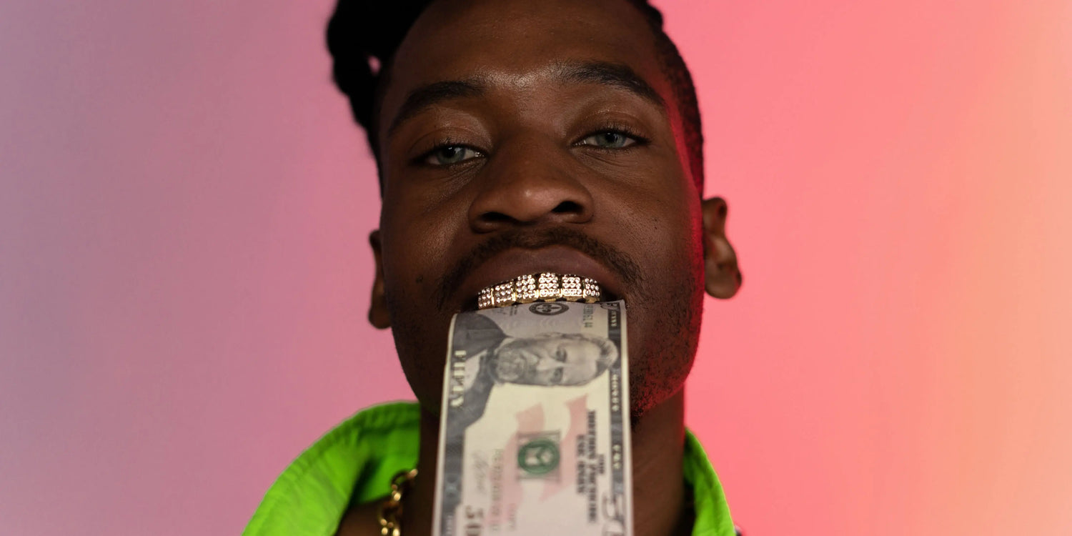 An artist is looking into the camera with grills and cash in his teeth