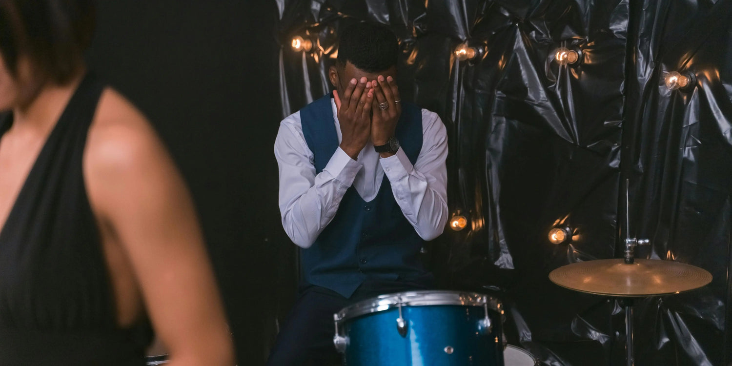 A drummer with his face in his hands looking frustrated