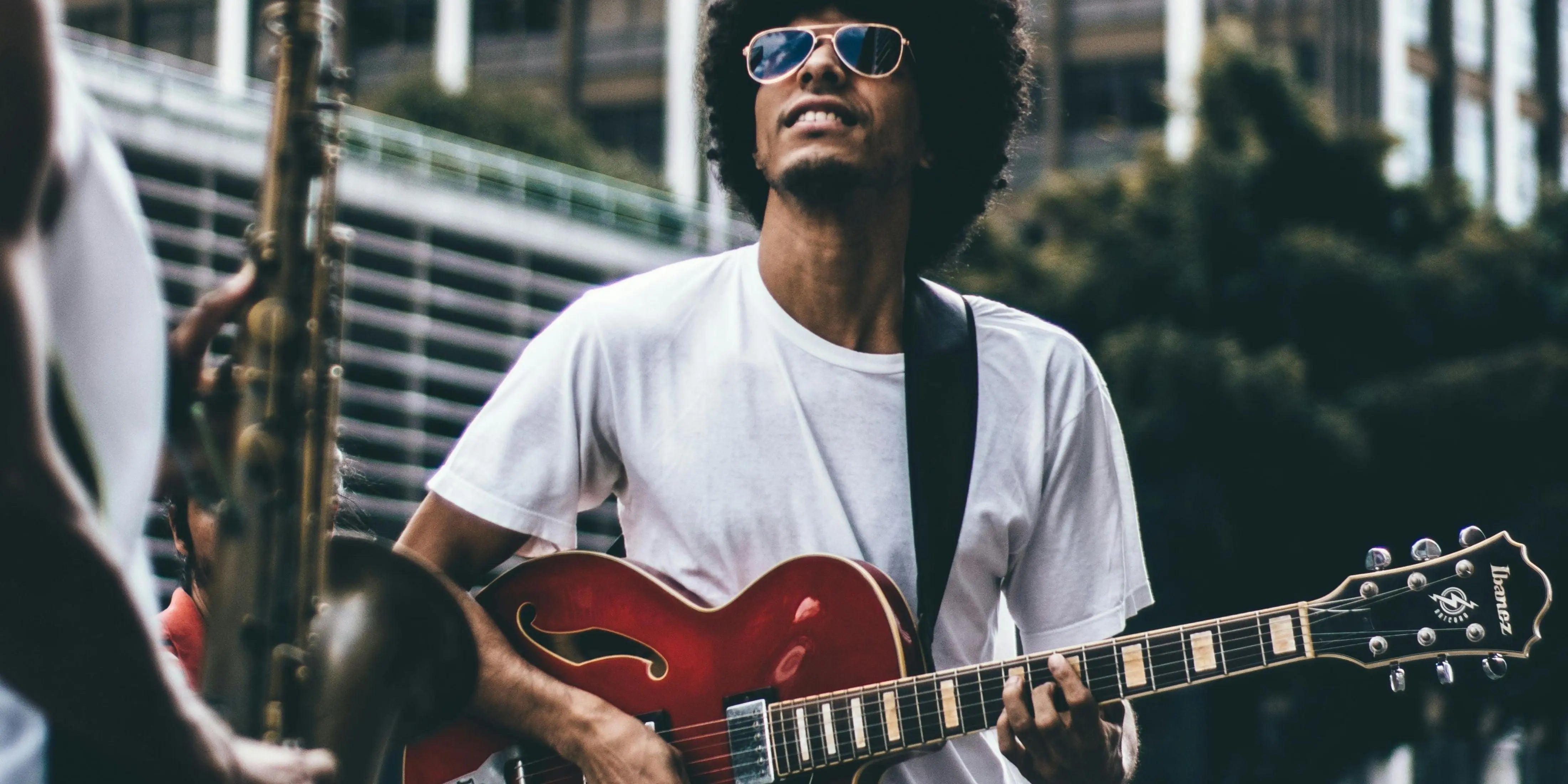 A young man playing a red guitar on the street