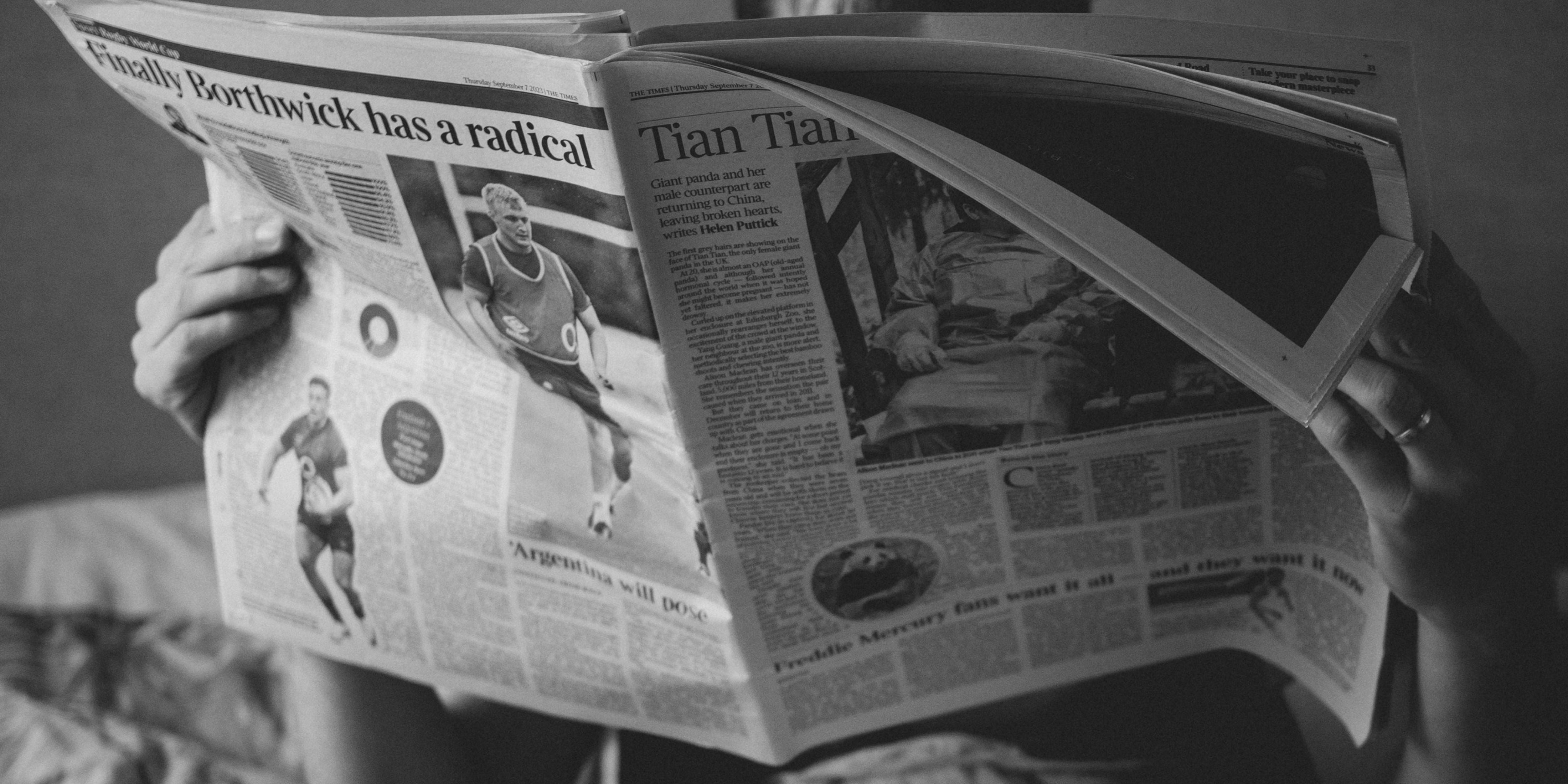 A man is reading a newspaper while sitting on his couch.