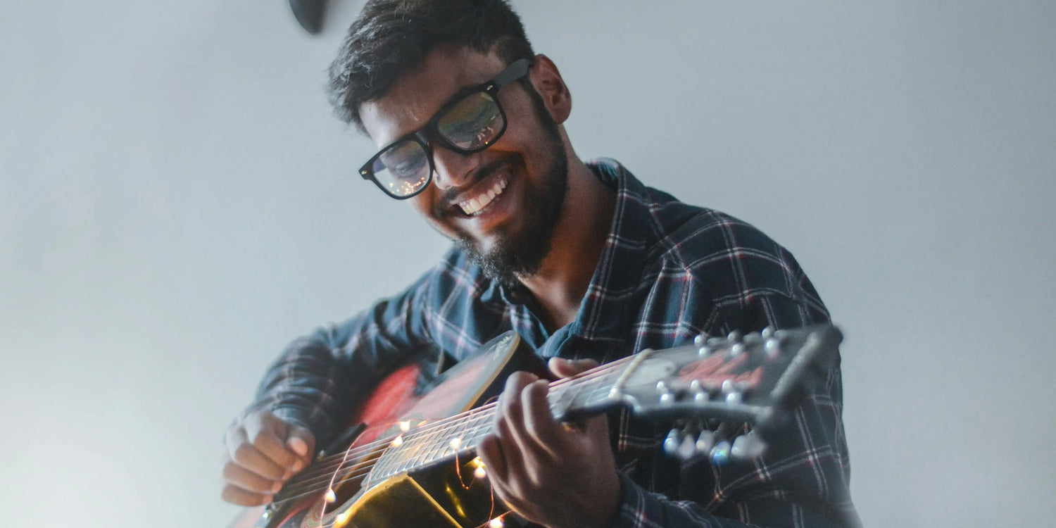 A musician is playing the guitar while sitting down and smiling.