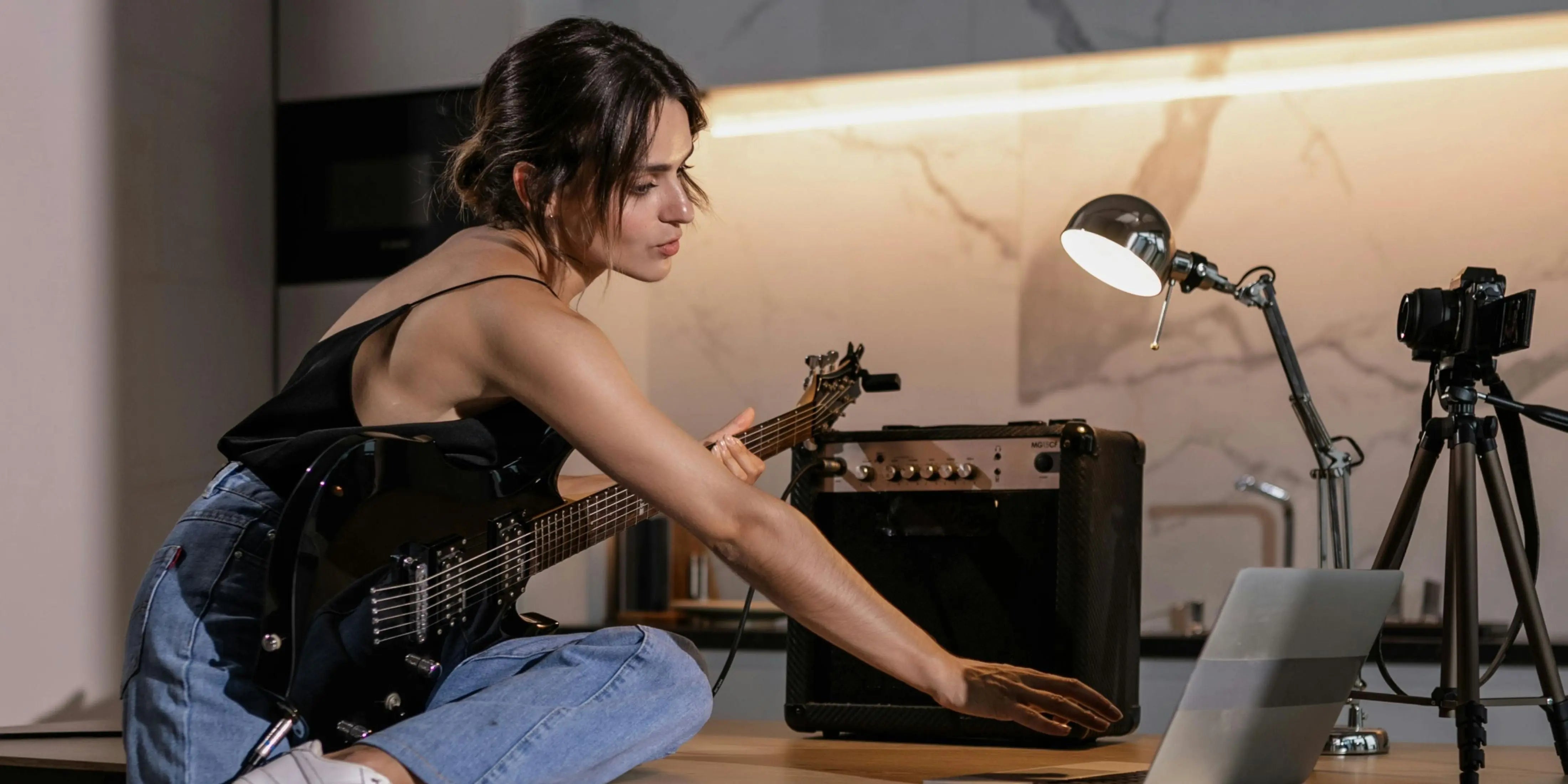 A musician is recording music on a guitar and laptop in the kitchen