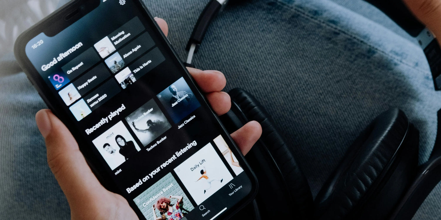 A man is holding his iPhone with Spotify playlists displayed on the screen.