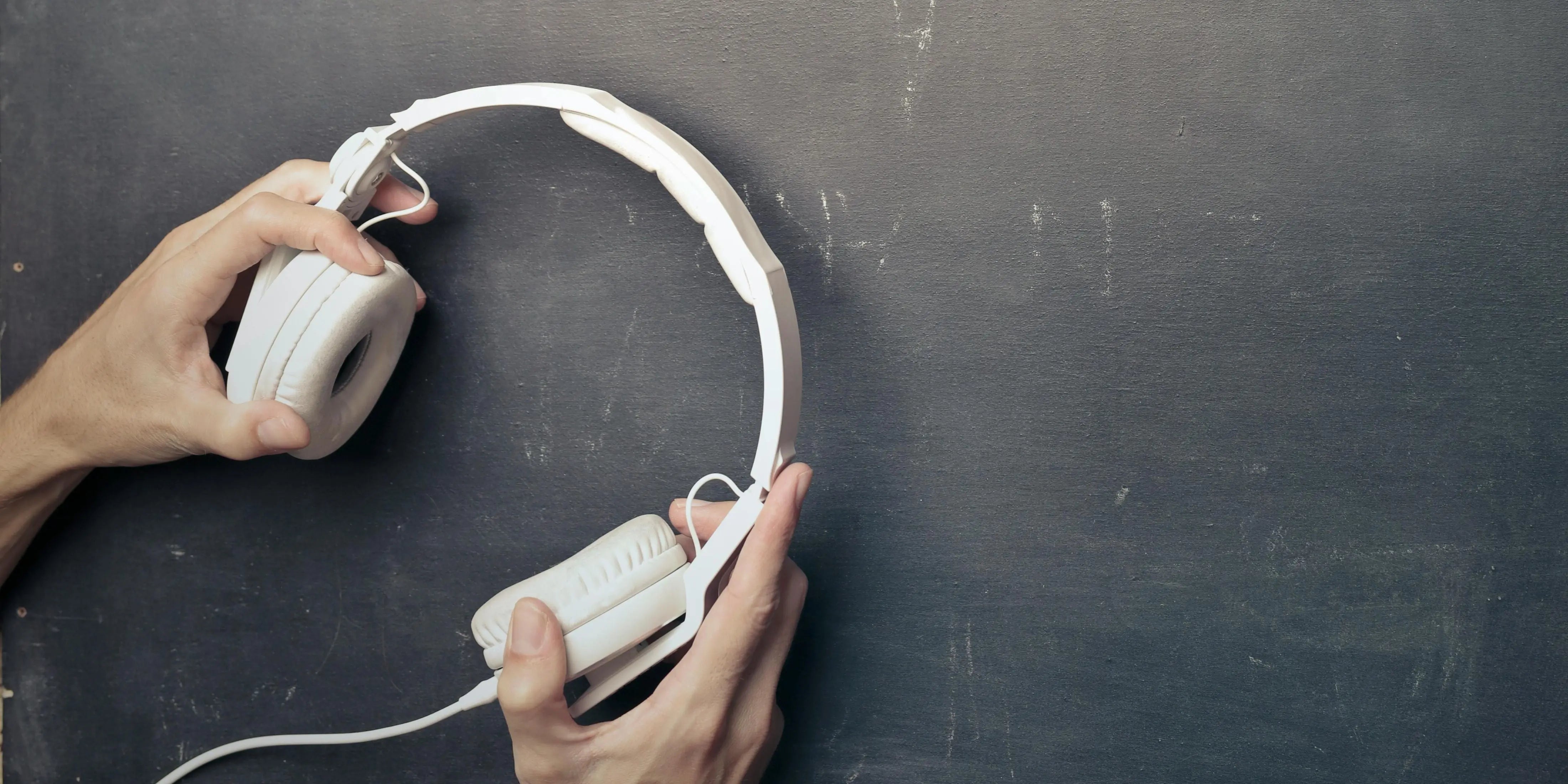 Two hands are holding a paid of white headphones