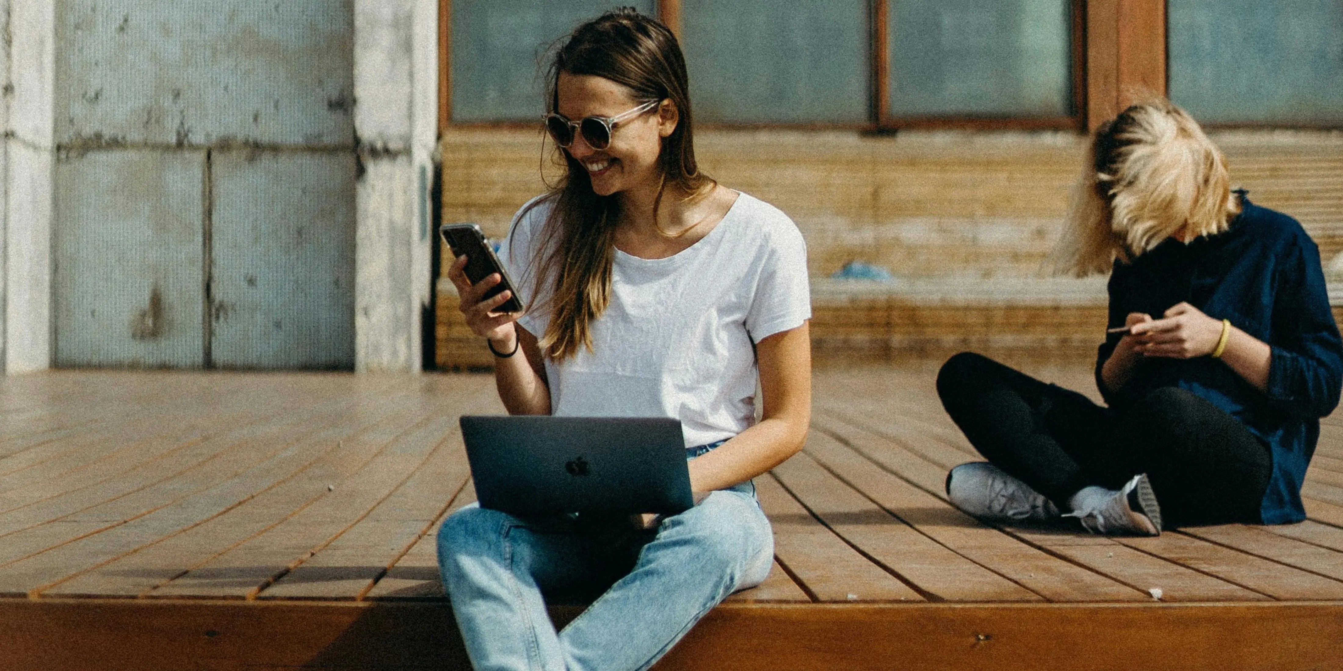 Two women are using their phones while sitting on wooden floor